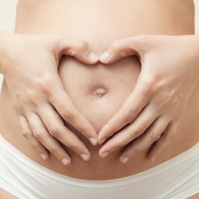Midsection Of Pregnant Woman Making Heart Shape Over Abdomen Against White Background